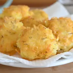 Frittelle di patate dorate e croccanti, condite con erbe aromatiche, servite su carta assorbente.