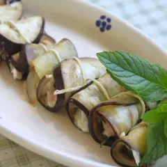 Deliziosi involtini di melanzane ripieni, guarniti con foglie di menta fresca su un piatto bianco.