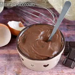Ciotola piena di deliziosa crema al cioccolato, con gusci d'uovo, frusta e tavolette di cioccolato.