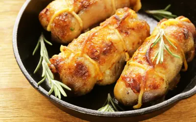 Involtini di pollo in padella, dorati e succulenti, con rametti di rosmarino fresco.