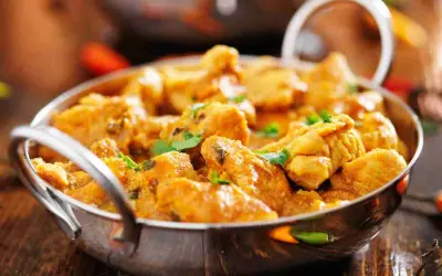 Un invitante pollo al curry cremoso, guarnito con coriandolo fresco, servito in una ciotola metallica su un tavolo di legno.