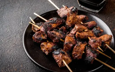 Spiedini di carne succulenti e grigliati, pronti per essere gustati con una salsa scura in un piattino.