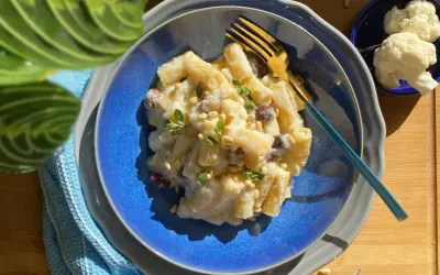 Creamy pasta with cauliflower, pine nuts, and herbs on a blue plate with a gold fork.