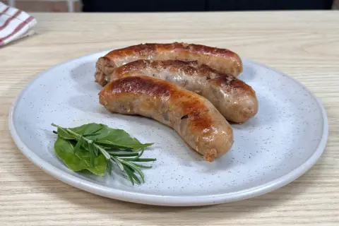 Tre succulente salsicce dorate in padella, servite su un piatto con rosmarino e alloro.