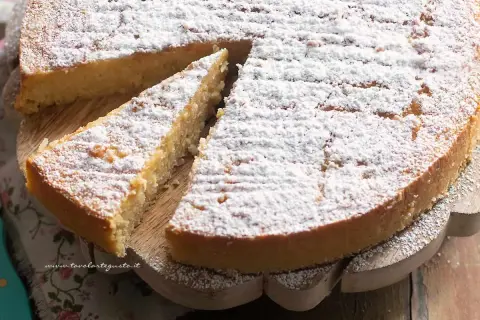 Una deliziosa torta di riso, cosparsa di zucchero a velo, su un tagliere di legno. Una fetta è già stata servita.