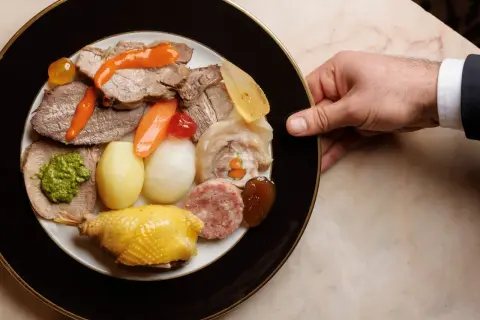 Piatto ricco con bollito di carne, pollo, salumi, verdure e salse, servito su un piatto elegante.