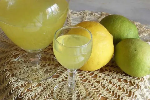 Limoncello ricetta originale Amalfi: bicchieri di liquore giallo brillante e limoni freschi, alcuni verdi, altri gialli, su un centrino di pizzo.