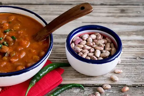 Un piatto fumante di fagioli alla messicana, con peperoncini verdi e una ciotola di fagioli crudi, pronti per un sapore piccante.