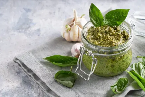 Vaso di vetro pieno di pesto fatto in casa, con aglio e basilico fresco. Perfetto per la pasta al pesto.