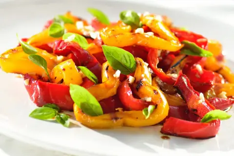 Peperoni arrostiti, rossi e gialli, conditi con aglio e basilico fresco. Un'idea gustosa per le tue ricette con peperoni.