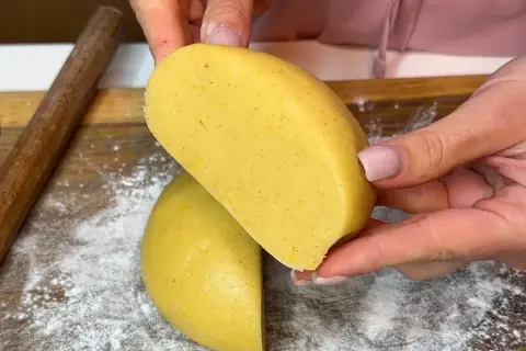 Mani che tengono un impasto giallo, profumato alla vaniglia, pronto per diventare una deliziosa pasta frolla senza burro.