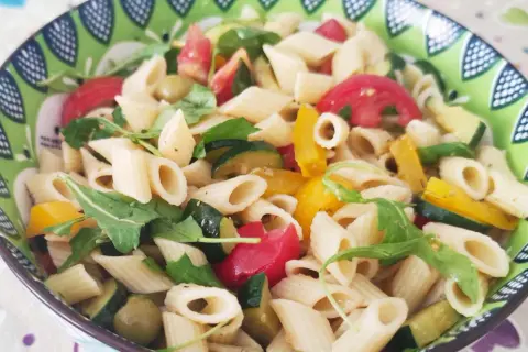 Un piatto colorato di pasta con verdure fresche: zucchine, pomodori, peperoni e rucola.