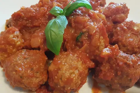 Polpette di carne morbide in un sugo rosso ricco, guarnite con foglie di basilico fresco.