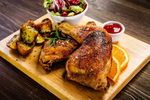 Un succulento arrosto di tacchino dorato, servito con patate arrosto, insalata fresca, salsa rossa e spicchi d'arancia su un tagliere di legno.
