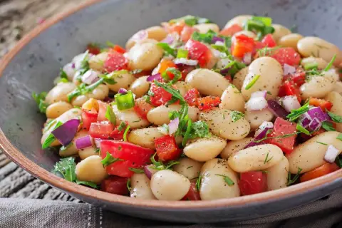 Insalata di fagioli bianchi, pomodori, cipolla rossa e erbe fresche, condita con spezie. Un piatto colorato e gustoso.