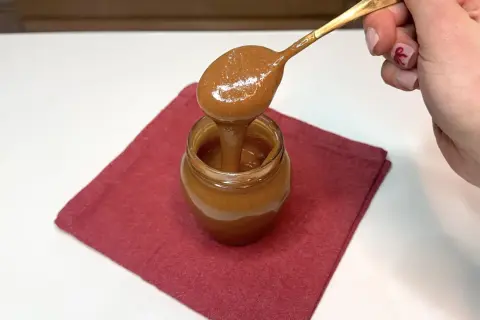 Un cucchiaio d'oro raccoglie un cremoso dulce de leche da un vasetto su un tovagliolo rosso.