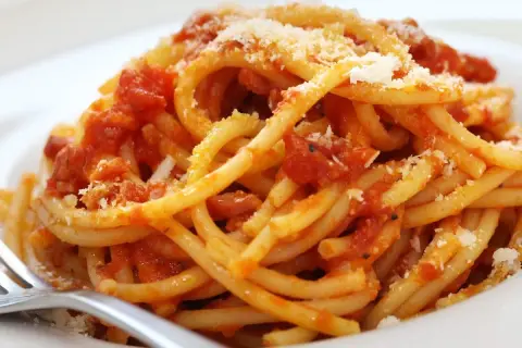 Un piatto di bucatini fumanti conditi con un ricco sugo all'amatriciana ricetta della nonna, spolverato di pecorino.