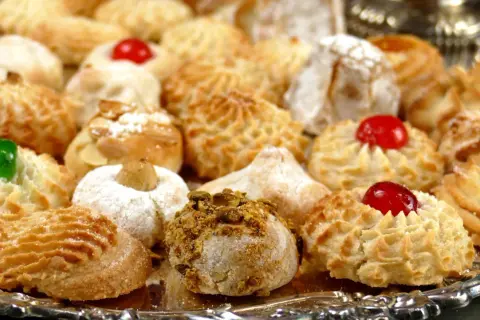 Vassoio pieno di biscotti alle mandorle, alcuni decorati con ciliegie rosse, mandorle e pistacchi.