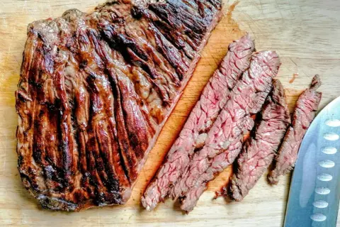 Diaframma di manzo grigliato, tagliato a fette sottili su un tagliere di legno. La carne è succulenta e ben cotta, con striature di grasso che la rendono ancora più invitante.