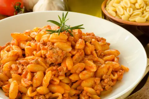 Un piatto invitante di malloreddus alla campidanese, conditi con un ricco sugo di carne e guarniti con rosmarino.