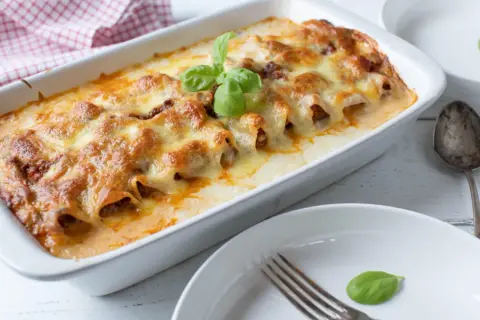 Cannelloni ripieni di carne macinata e mozzarella, cotti al forno e gratinati, guarniti con basilico fresco.