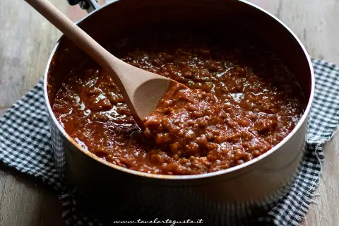 Un pentolone pieno di ragù alla bolognese, pronto per condire la pasta. Un cucchiaio di legno mescola la salsa ricca e saporita.