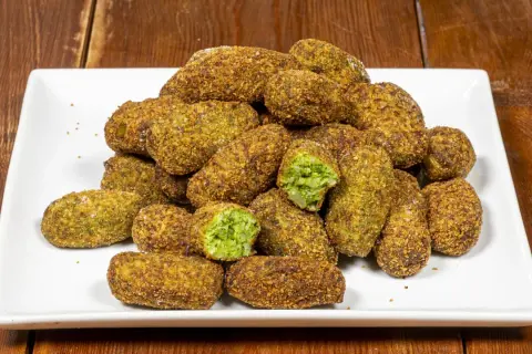 Un mucchio di polpette di broccoli dorate e croccanti su un piatto bianco. Alcune sono tagliate a metà, rivelando il ripieno verde brillante.