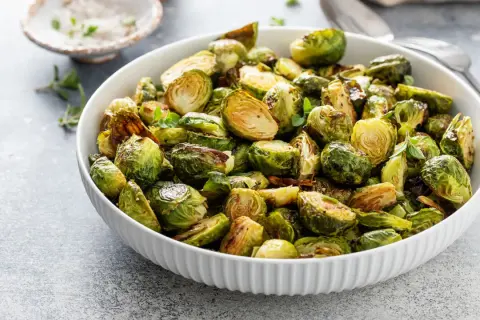 Ciotola piena di cavoletti di Bruxelles arrostiti, dorati e saporiti, guarniti con erbe fresche.