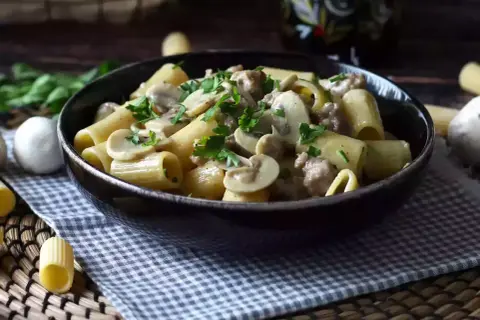 Piatto fumante di pasta funghi e salsiccia, guarnito con prezzemolo fresco. Un classico confortante.