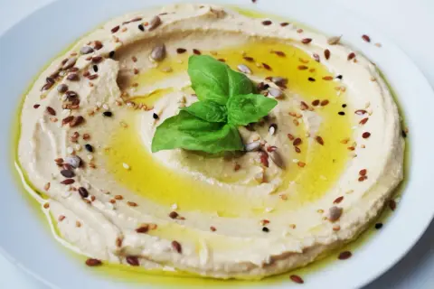 Cremoso hummus di ceci, condito con olio d'oliva, semi misti e una foglia di basilico fresco.