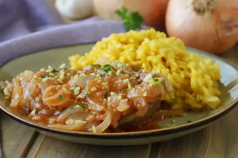 Un succulento ossobuco alla milanese, tenero e saporito, servito con un cremoso risotto giallo.