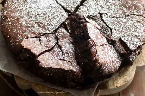 Una deliziosa torta al cioccolato fondente, con una crosta crepata e cosparsa di zucchero a velo, pronta per essere gustata.