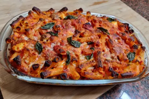 Un invitante piatto di pasta al forno napoletana, con pasta rigata dorata, sugo rosso e formaggio fuso, guarnito con foglie di basilico fresco.