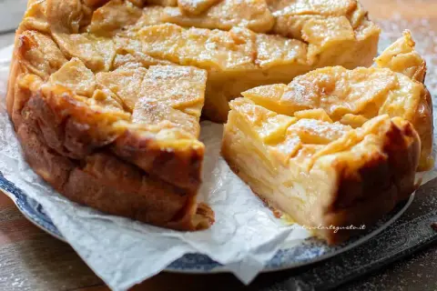 Una deliziosa torta di mele dorata, con fette di mela caramellate in superficie e una spolverata di zucchero a velo.