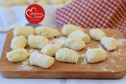 Gnocchi di ricotta freschi, pronti per essere cucinati, spolverati di farina su un tagliere di legno.