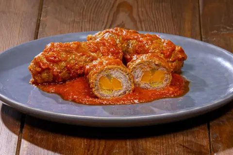 Involtini alla romana succulenti, avvolti in un sugo rosso intenso, con un cuore dorato visibile in sezione.