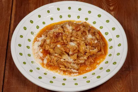 Un piatto di trippa alla fiorentina, saporita e ricca, cosparsa di parmigiano grattugiato, servita su un piatto bianco decorato.