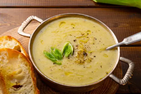 Una ciotola di cremosa crema di patate, guarnita con cipollotto fresco e pepe nero, servita con fette di pane tostato.