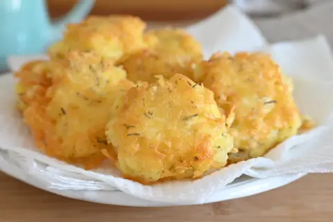 Frittelle di patate dorate e croccanti, condite con erbe aromatiche, servite su carta assorbente.
