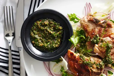 Costolette d'agnello con salsa verde senza uovo, servite su un letto di finocchio e cipolla rossa.