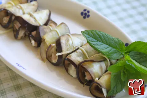 Deliziosi involtini di melanzane ripieni, guarniti con foglie di menta fresca su un piatto bianco.