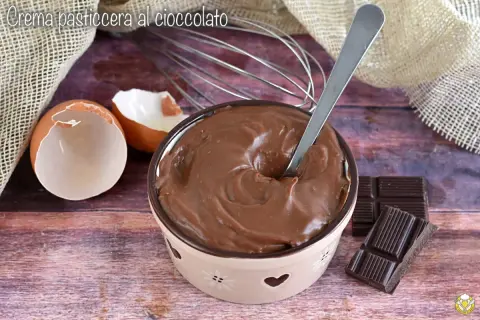 Ciotola piena di deliziosa crema al cioccolato, con gusci d'uovo, frusta e tavolette di cioccolato.