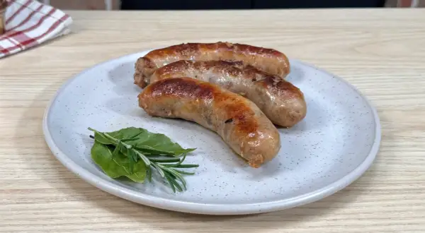 Tre succulente salsicce dorate in padella, servite su un piatto con rosmarino e alloro.