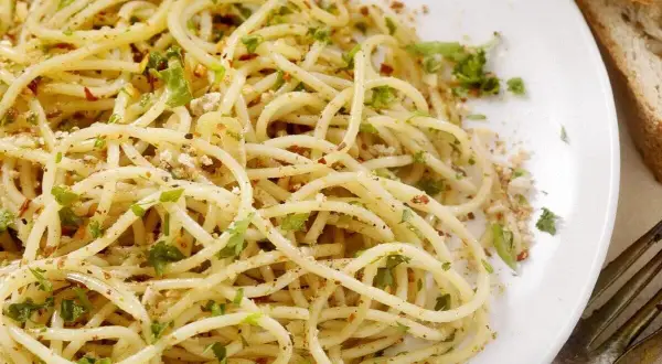 Un piatto di spaghetti alla carrettiera, conditi con aglio, olio, peperoncino e prezzemolo fresco, accompagnati da pane rustico.