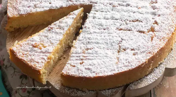 Una deliziosa torta di riso, cosparsa di zucchero a velo, su un tagliere di legno. Una fetta è già stata servita.