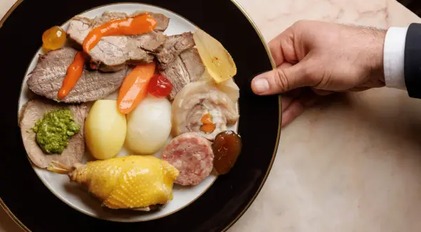 Piatto ricco con bollito di carne, pollo, salumi, verdure e salse, servito su un piatto elegante.