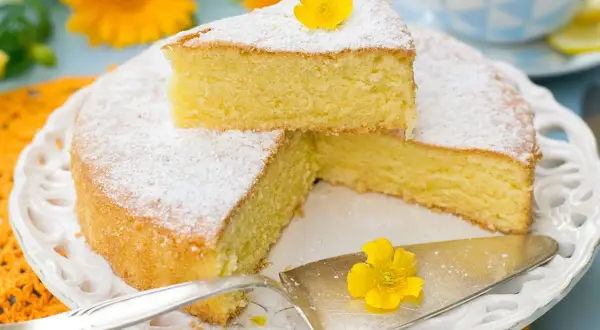 Una torta paradiso sofficissima, spolverata di zucchero a velo e decorata con un fiore giallo, pronta per essere gustata.
