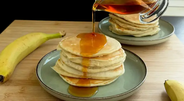 Pancake alla banana con sciroppo d'acero che cola su una pila di soffici pancake.