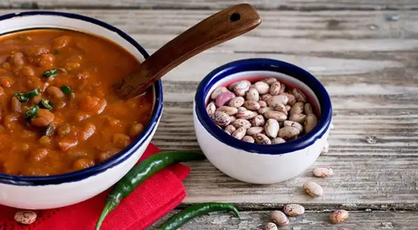 Un piatto fumante di fagioli alla messicana, con peperoncini verdi e una ciotola di fagioli crudi, pronti per un sapore piccante.