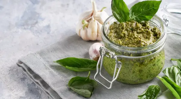 Vaso di vetro pieno di pesto fatto in casa, con aglio e basilico fresco. Perfetto per la pasta al pesto.